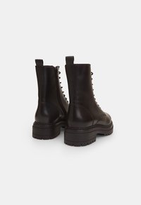 Bottes courtes en cuir noir avec bout arrondi, fermeture éclair latérale et devant à lacets. Semelle en caoutchouc épaisse avec détails texturés. Fini lisse.