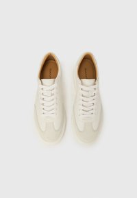 Λευκά δερμάτινα αθλητικά παπούτσια με λείο φινίρισμα και διάτρητο σχέδιο. Διαθέτουν επίπεδα κορδόνια, ελαστική σόλα και μπεζ εσωτερική επένδυση.