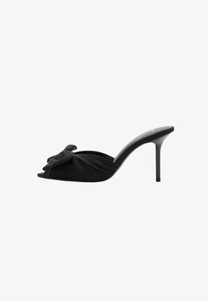 Mules negros de punta abierta con un alto tacón de aguja. Presentan un detalle de lazo anudado en un tejido suave y un diseño contorneado y liso.