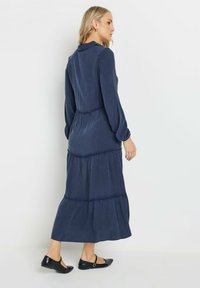 Mörkblå lager-på-lager maxiklänning i mjukt tyg med krage och långa ärmar. Har infällda sömmar och en svävande silhuett.