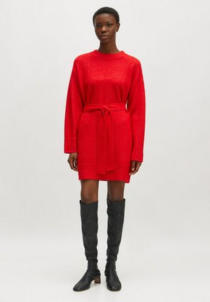 Rotes Strickkleid mit langen Ärmeln und gebundenem Gürtel, mit einer strukturierten Oberfläche und lockerer Passform. Kombiniert mit knielangen schwarzen Stiefeln.
