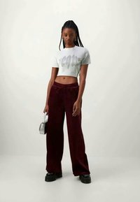 Tricou scurt de culoare gri deschis cu literă reliefată, asociat cu pantaloni largi de culoare burgundy și pantofi cu talpă înaltă negri. Posetă mică din silver.