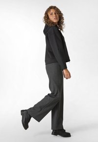 Schwarzer Kapuzenpullover mit lockerer Passform, kombiniert mit grauen Karottenhosen und schwarzen Schnürstiefeln. Das Outfit hat einen lässigen, aber dennoch strukturierten Look.