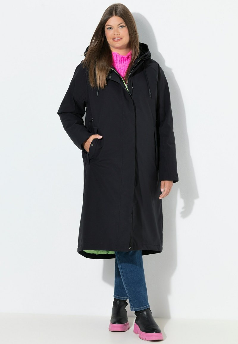 Černý voděodolný kabát s kapucí, plné délky, boční kapsy, spárovaný se zářivě růžovým svetrem a černými džínami, doplněný o růžové masivní boty.
