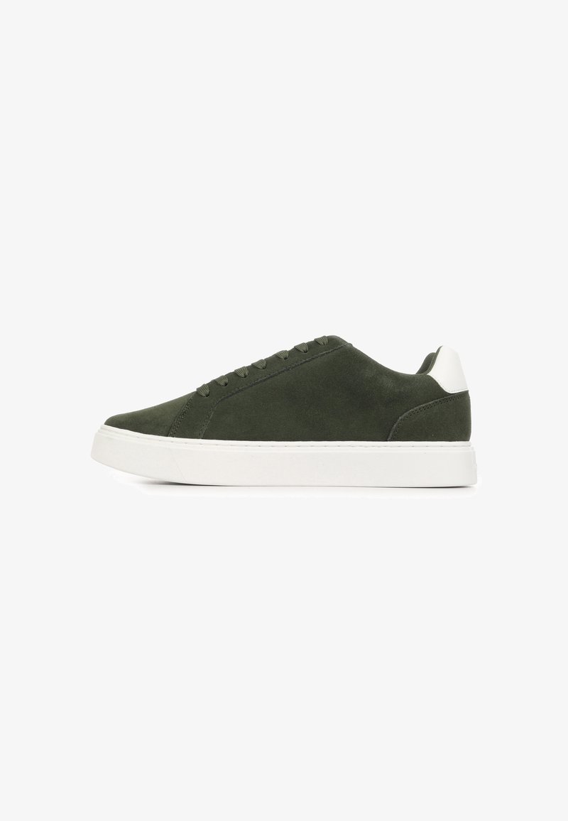 Baskets basses en daim vert foncé avec semelle blanche et languette au talon, fermeture à lacets, et design minimaliste sur fond blanc.