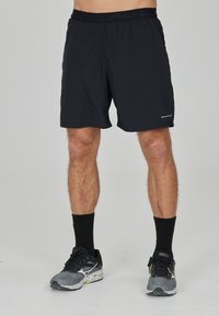 Schwarze Sportshorts aus leichtem Material mit elastischem Bund. Dazu schwarze Socken und graue Laufschuhe mit gelben Akzenten.