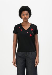 Schwarzes Baumwoll-T-Shirt mit kurzen Ärmeln und V-Ausschnitt, das auf der Vorderseite rote gestickte Herzen in unterschiedlichen Größen zeigt.