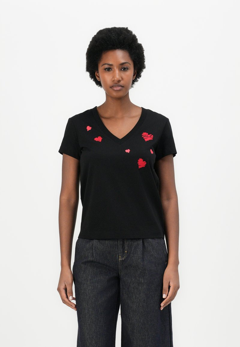 Schwarzes Baumwoll-T-Shirt mit kurzen Ärmeln und V-Ausschnitt, das auf der Vorderseite rote gestickte Herzen in unterschiedlichen Größen zeigt.