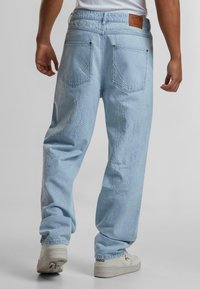 Blugi din denim albastre deschise cu broderie în model de flacără, croi relaxat, talie elastică și patch cu logo pe spate. Adidași albi.