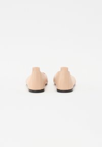 Ballerines en cuir nude avec une finition lisse, bout arrondi et petit talon noir, présentant un design minimaliste sans quincaillerie visible.