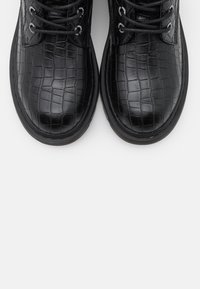 Bottes en cuir noir à lacets avec une texture crocodile, bout rond et œillets en métal pour les lacets, dotées d'une semelle en caoutchouc noir lisse.