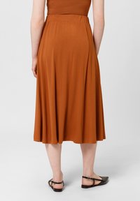 Jupe marron, longueur genou, à taille élastique, fabriquée en tissu doux ; présente un design fluide et une texture lisse, assortie à des sandales noires simples.