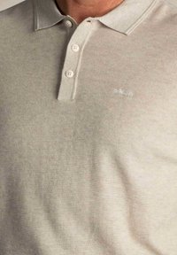 Lichtbeige polo-shirt met een textuurpatroon, voorzien van een opstaande kraag, drie knopen en een discreet geborduurd logo in het midden.