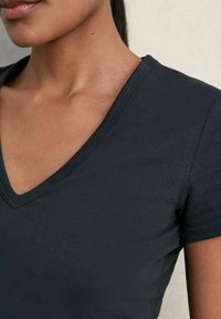 Tricou negru cu decolteu în V, realizat din bumbac neted, cu mâneci scurte. Vedere de aproape care evidențiază decolteul și textura materialului.
