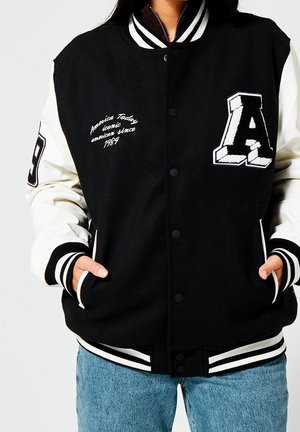 Giacca varsity bianca e nera con maniche a contrasto, polsini a coste e scritte ricamate sulla parte anteriore, con bottoni a pressione.