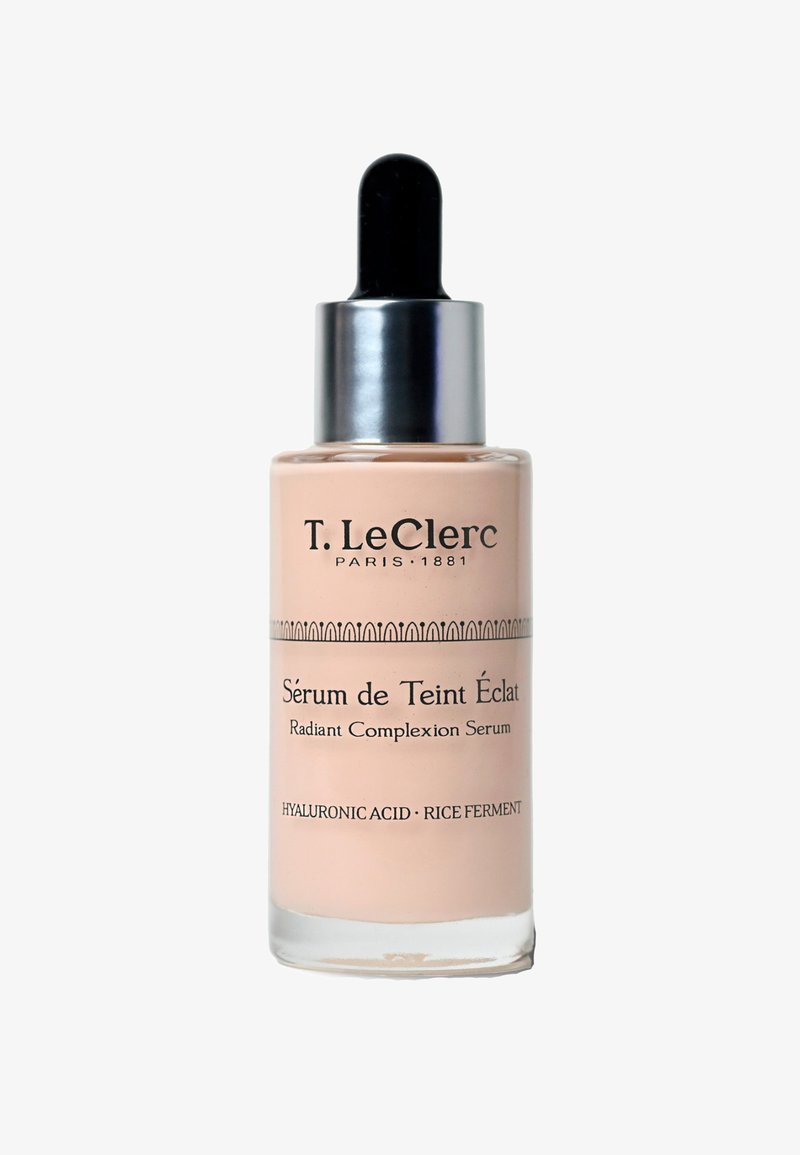 Strahlendes Teint-Serum in einer klaren Glasflasche mit einem schwarzen Tropfer. Enthält eine pfirsichfarbene Flüssigkeit und Details in Schwarz und Silber.