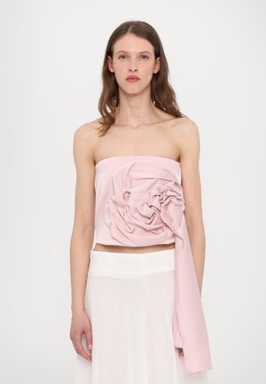 Stoffoberteil ohne Träger in zartem Rosa mit einem großen, drapierten Blumendetail auf der Vorderseite und glatter Textur, kombiniert mit einem durchsichtigen weißen Rock.