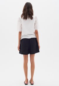 Bílá tričko s vyšitými očky a nabíranými rukávy, spárované s černými šortkami s volným střihem a jemným výřezem.