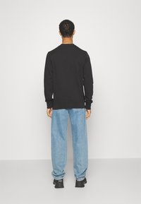 Zwarte crewneck-trui met geribde manchetten, gecombineerd met lichtblauwe wijde spijkerbroek en zwarte sneakers. Eenvoudige, minimalistische achteraanzicht.