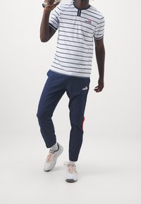 Vit och marinrandig kortärmad skjorta med henleykrage, tillsammans med marinblå joggers med röda detaljer och vita sneakers.