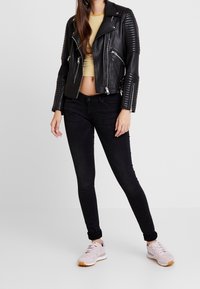 Zwarte leren motorjack met geïsoleerde schouders, gecombineerd met een gestreepte crop top, zwarte jeans en lichtroze sneakers.