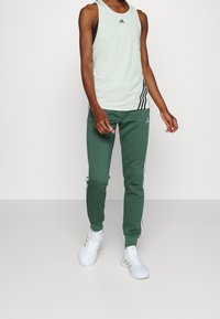 Ljust grön ärmlös linne med svarta accenter, parat med mörkgröna joggers med vita sidostråk. Bärs med vita sneakers.