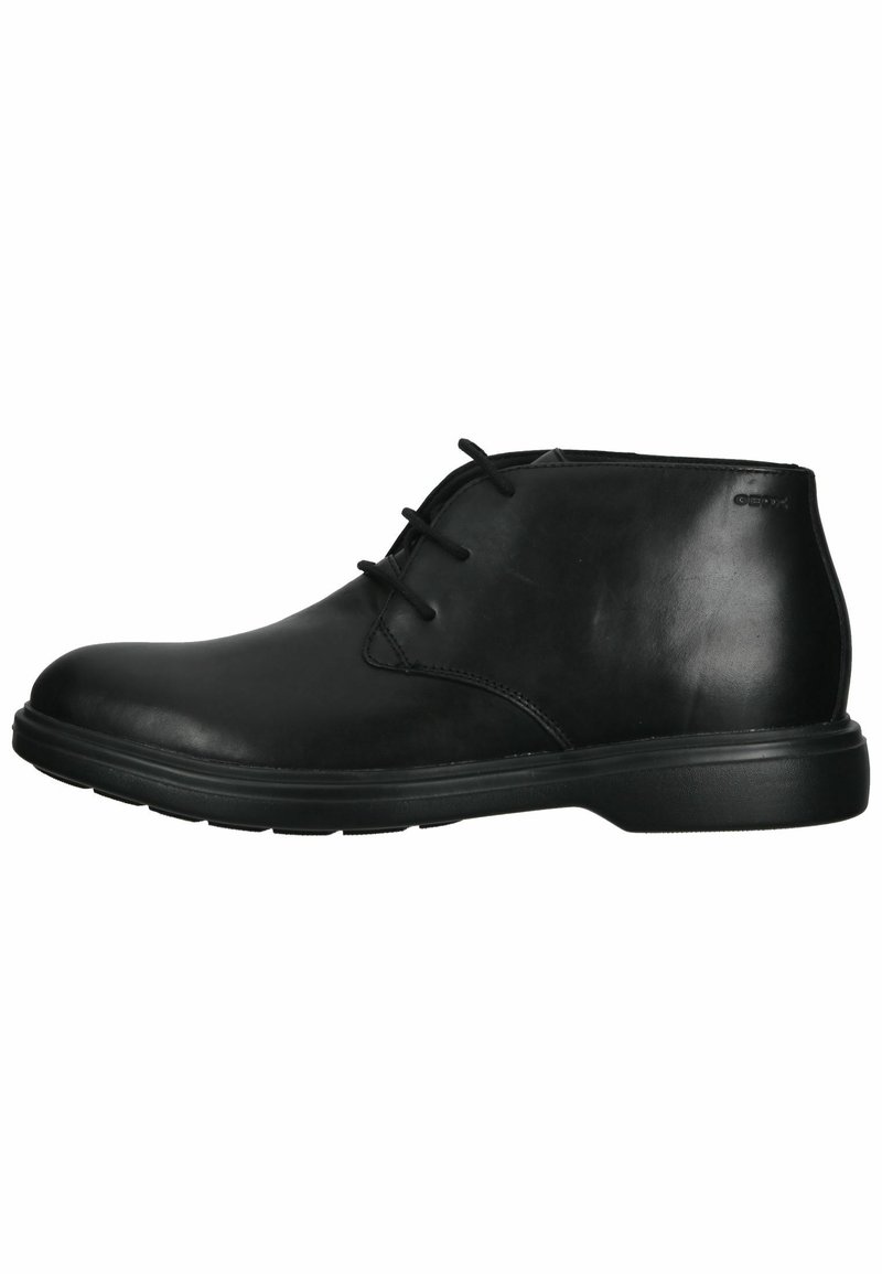 Bottes noires en cuir avec bout rond, trois œillets et semelle en caoutchouc. Texture lisse avec un subtil détail de couture sur les côtés.