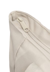 Beige szövet táska sarka, texturált felülettel, cipzáros záródással és kis húzófüllel. Látható a varrott varrás részlete.