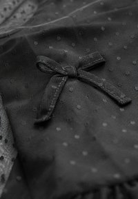 Svart tylltyg med prickmönster, prytt med en liten svart rosett. Mjuk textur med fransade kanter.