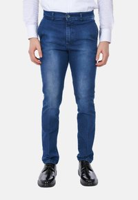 Jeans in denim blu con vestibilità slim, caratterizzati da chiusura con bottone, tasche frontali e dettagli sbiaditi. Abbinati a scarpe eleganti nere.