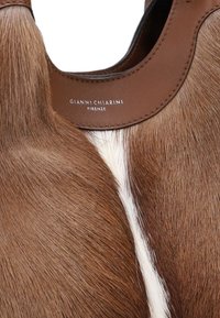 Borsa a mano in pelle marrone con texture in pelliccia, un accento liscio e un'etichetta logo visibile impressa sul collo in pelle marrone.