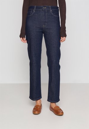Straight-leg mørkeblå denimjeans båret med brune loafers og en mørkebrun top med lange ærmer, vist fra talje til fødder.