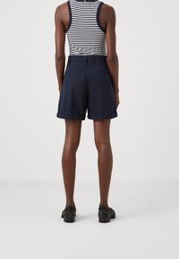 Granatowe szorty z podwiniętymi nogawkami i tylnymi kieszeniami, w połączeniu z czarną i białą pasiastą bluzką bez rękawów, widok z tyłu.