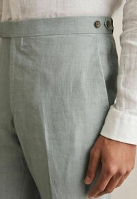 Világosszürke len nadrág, egyenes szabással, lapos elülső részel, két gombbal a derékpánton, és finom textúrával az anyagban.