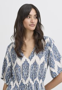 Geprinte jurk met een V-hals, met een blauw-witte bloemenontwerp. Korte mouwen, getailleerde taille met aantrekkoord, gemaakt van lichtgewicht stof.