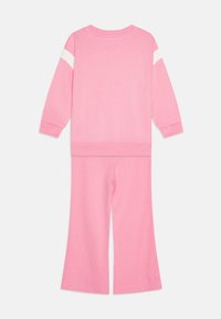 Pink sweat outfit consisting of a long-sleeve top with white stripes on sleeves and flared pants. Material appears soft and textured.