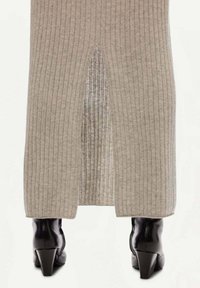 Grå ribbad midikjol med en frontslits, i kombination med svarta klackade ankellånga stövlar. Tyget har en strukturerad, mysig look.