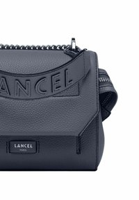 Borsa a tracolla in pelle grigia con texture, caratterizzata da un logo in rilievo prominente, dettagli in catena argentata e una cerniera laterale. Forma rettangolare compatta.
