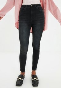 High-waisted black skinny jeans with a smooth denim texture, five pockets, and a front button closure, paired with black textured loafers.