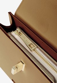 Beige Leder-Wallet-Innenraum mit goldenen Beschlägen. Verfügt über ein weißes, mit Reißverschluss versehenes Fach und eine strukturierte Oberfläche. Auffälliges Branding-Detail sichtbar.