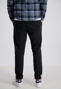 Svarta joggerbyxor med en mjuk textur, slim fit-design och elastisk midja, kombinerat med vita sneakers och en blå rutig skjorta.