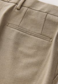 Pantalon en tissu beige avec motif à fines rayures verticales, deux poches arrière, et une texture lisse avec un éclat subtil.