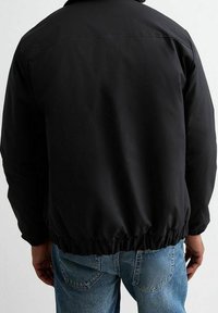 Czarna lekka kurtka typu bomber z elastycznym dołem i gładką fakturą, z długimi rękawami i prostym, minimalistycznym wzorem.