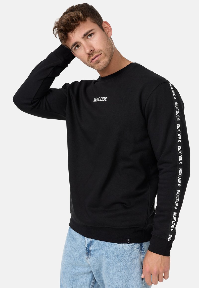 Sweatshirt noir avec col rond et manches longues. Présente le logo blanc "INDICODE" sur la poitrine et la manche. Tissu doux et coupe décontractée.