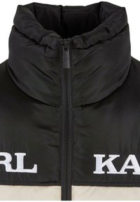 Juodas pūkuotas švarkas su aukštu apykakle, pilnu užtrauktuku ir ryškiu baltu "KARL" logotipu priekyje. Lygus, blizgus audinio paviršius.