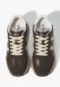 Brązowe sportowe sneakersy z mieszanką matowych i błyszczących tekstur, beżowymi sznurówkami i trzema białymi pasami po bokach. Minimalistyczny design z zaokrąglonym czubkiem.