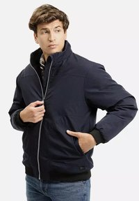 Granatowa pikowana kurtka z wysokim kołnierzem, z zapięciem na zamek z przodu oraz kieszeniami po bokach. Posiada ściągacze na rękawach i teksturowaną fakturę materiału.