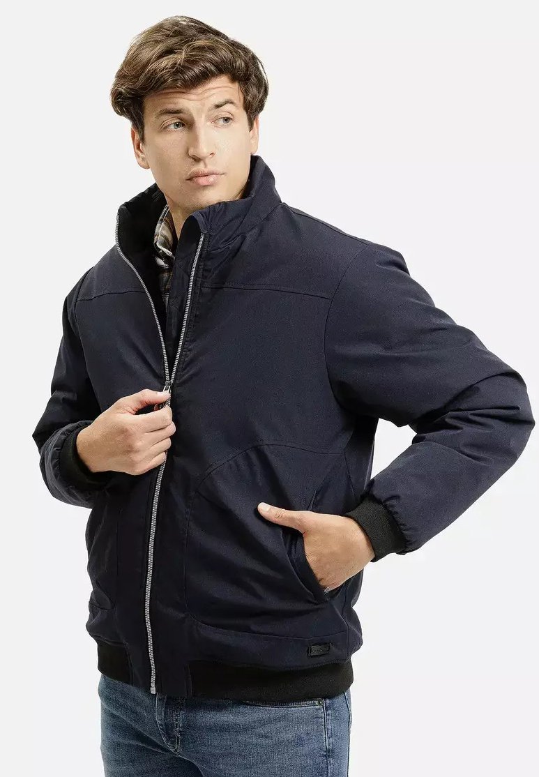 Granatowa pikowana kurtka z wysokim kołnierzem, z zapięciem na zamek z przodu oraz kieszeniami po bokach. Posiada ściągacze na rękawach i teksturowaną fakturę materiału.