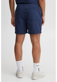 Granatowe szorty z teksturowanej tkaniny, elastycznym pasem i tylną kieszenią. Noszone z białymi skarpetkami i jasnozłotymi sneakersami.