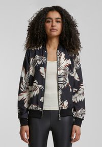 Veste bomber noire avec un grand motif de feuilles tropicales blanches et brunes. Tissu lisse avec une fermeture éclair et des poignets côtelés.